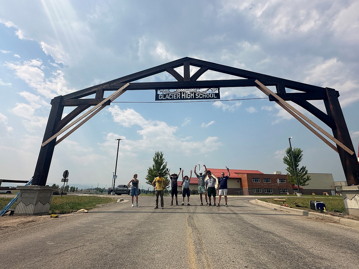 Glacier High School staff and students celebrate after a student-built truss over a parking lot entrance on Thursday, July 18. The truss was built by the Outdoor Art class during the 2023-24 school year. To preserve the timber, a Japanese technique called shou sugi ban was used where the wood was charred with a torch and wire brushes were used to stain it. Pictured left to right: student Mandie Manning, art teacher C.J. Cummings, art teacher Eric Hanson, John Cummings, art teacher Josh Mohler,  Assistant Principal and Activities Director Mark Dennehy and Principal Brad Holloway. (Photo provided by C.J. Cummings)