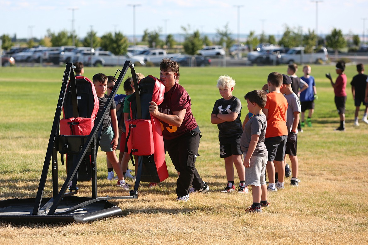 A Moses Lake High School football player teaches the youth campers how to use the blocking sled during a drill on Tuesday.