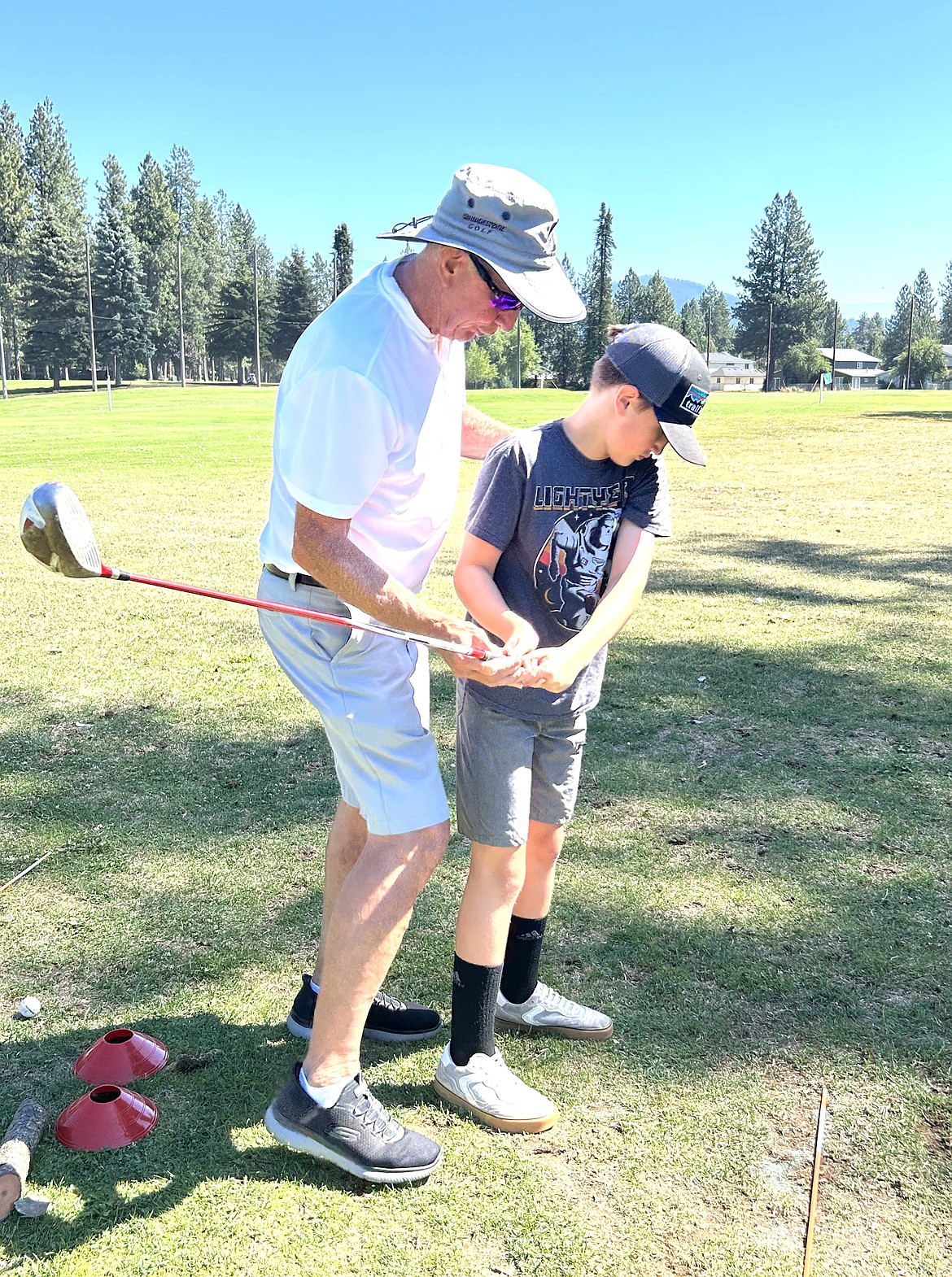 Volunteer Dick Schultz with Friends of CDA Public Golf Club Foundation helps Larsen Pichotta during a golf lesson at the Coeur d'Alene Public Golf Club on Thursday.