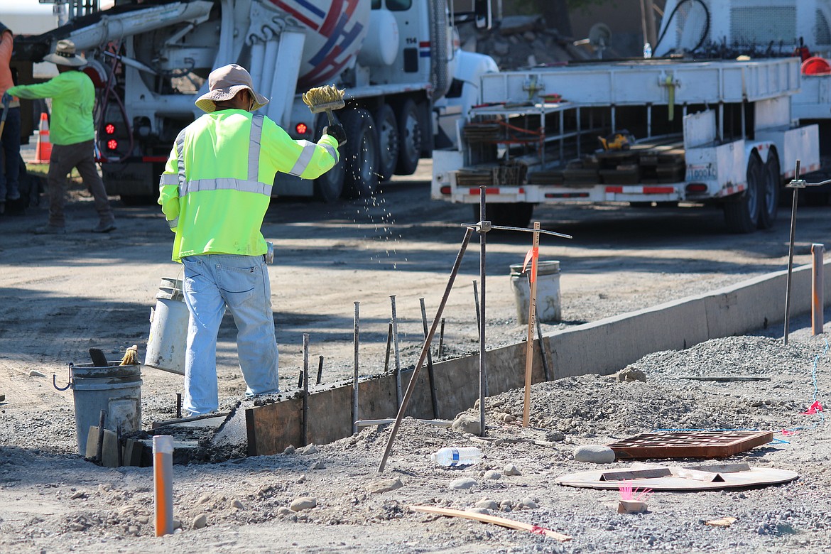 A construction worker splashes water on a still-drying concrete curb.