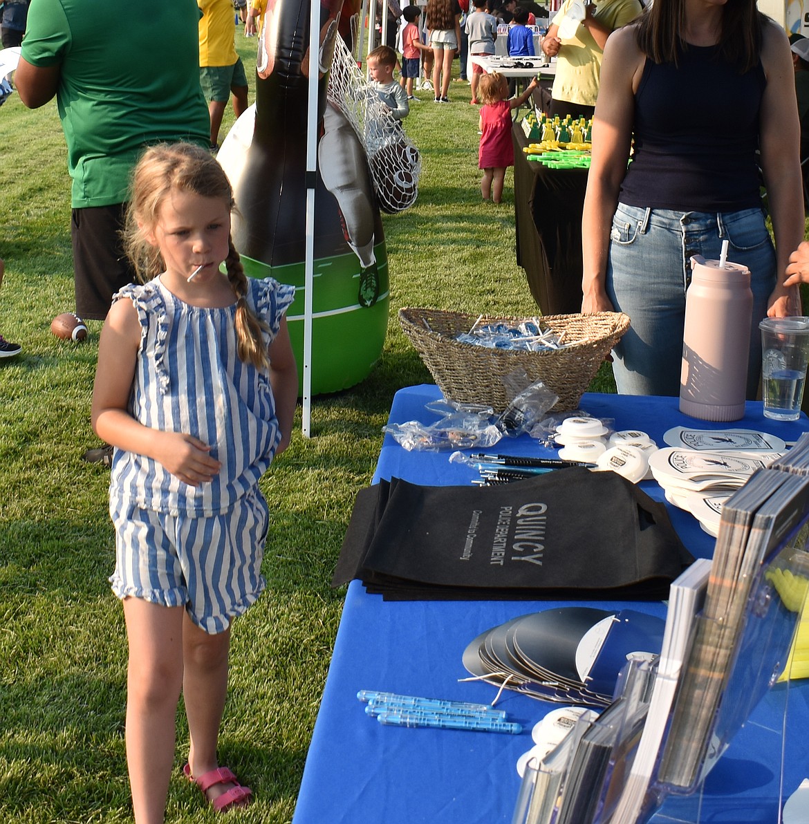 Greta Glatz, 7, checks out the swag at the Quincy Police Department’s booth at National Night Out Monday. The children love the giveaways, some exhibitors said, but that leads the adults with them into conversations with law enforcement and firefighters.