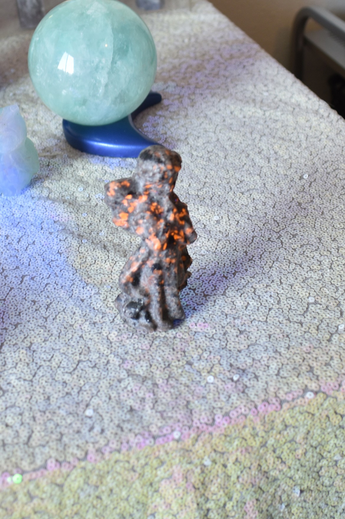 Tia Seibel shines an ultraviolet light on a figure of an angel, causing parts of it to glow orange. The angel is made of yooperlite, a mineral crystal found in Michigan’s upper peninsula.