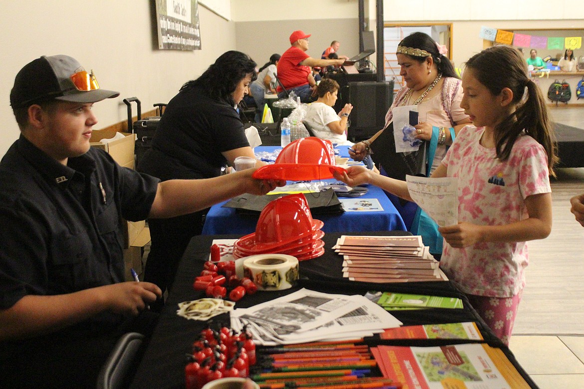 A child at the Quincy Back to School Health Fair gets her own fire hat from Grant County Fire District 3 volunteers.