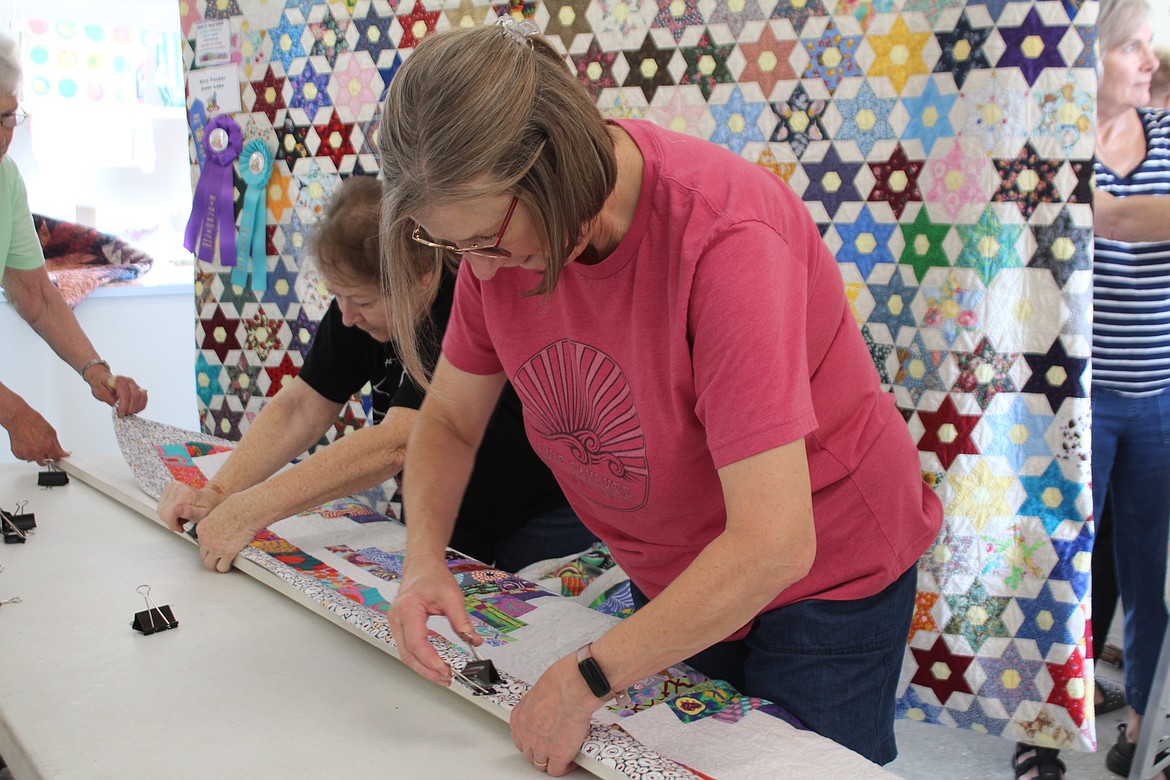 Volunteers Kathy Kalamakis, left, and Kim Garza, right, prepare a quilt for hanging in the Grant County Fair quilt show.