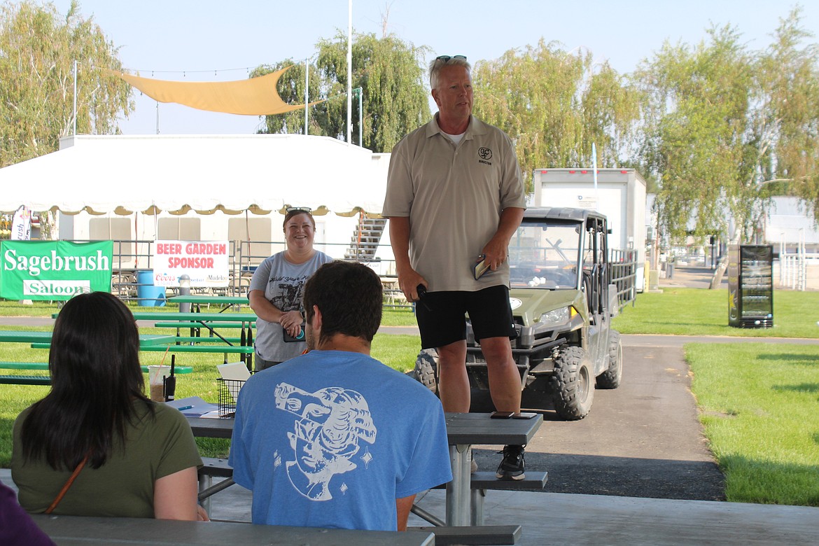 Perched on a picnic table, Grant County Fairgrounds manager Jim McKiernan addresses volunteers during orientation.