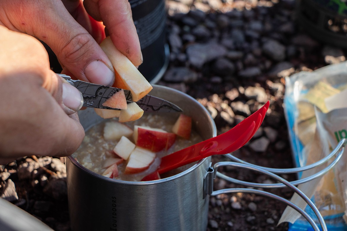 Brandon Phillips cuts an apple into his oatmeal for breakfast during a backpacking trip. (Kate Heston/Daily Inter Lake)