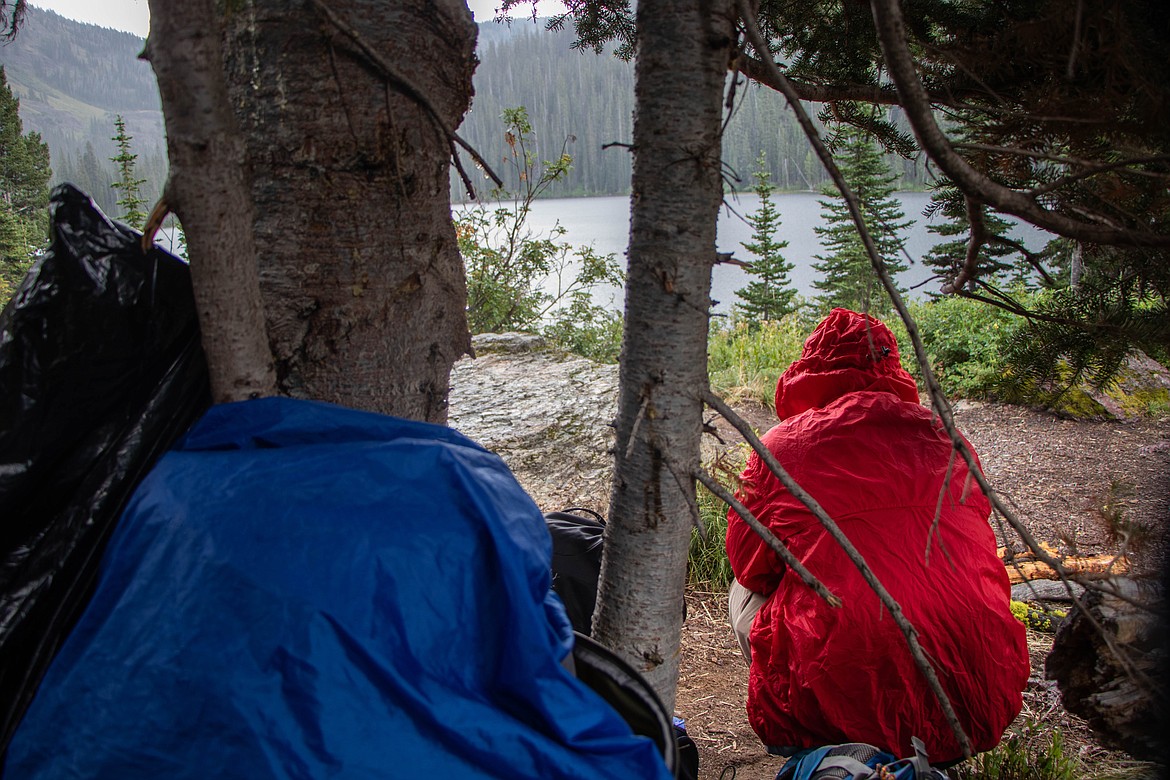 Ron Rydelle Ramos, from Hawaii, waits out the storm under a tree on a backpacking trip. (Kate Heston/Daily Inter Lake)