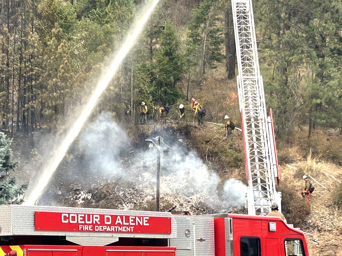 Firefighters spray water on the Wolf Lodge Steakhouse, while Idaho Department of Lands crews dig a fire line on the hillside to the east of the restaurant on Monday.