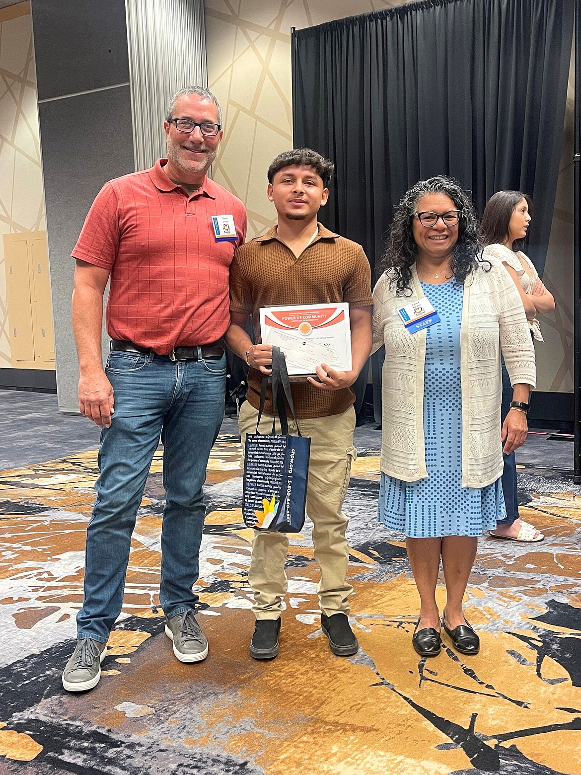 Community Health Plan of Washington Regional Manager Daniel Smith, left, and OSPI Migrant Education Program Director Sylvia Reyna present Haziel Sandoval-Gatica with the 2024 CHPW Power of Community Perseverance Award, in recognition of his perseverance in finishing high school, determination to succeed and involvement in extracurricular activities.