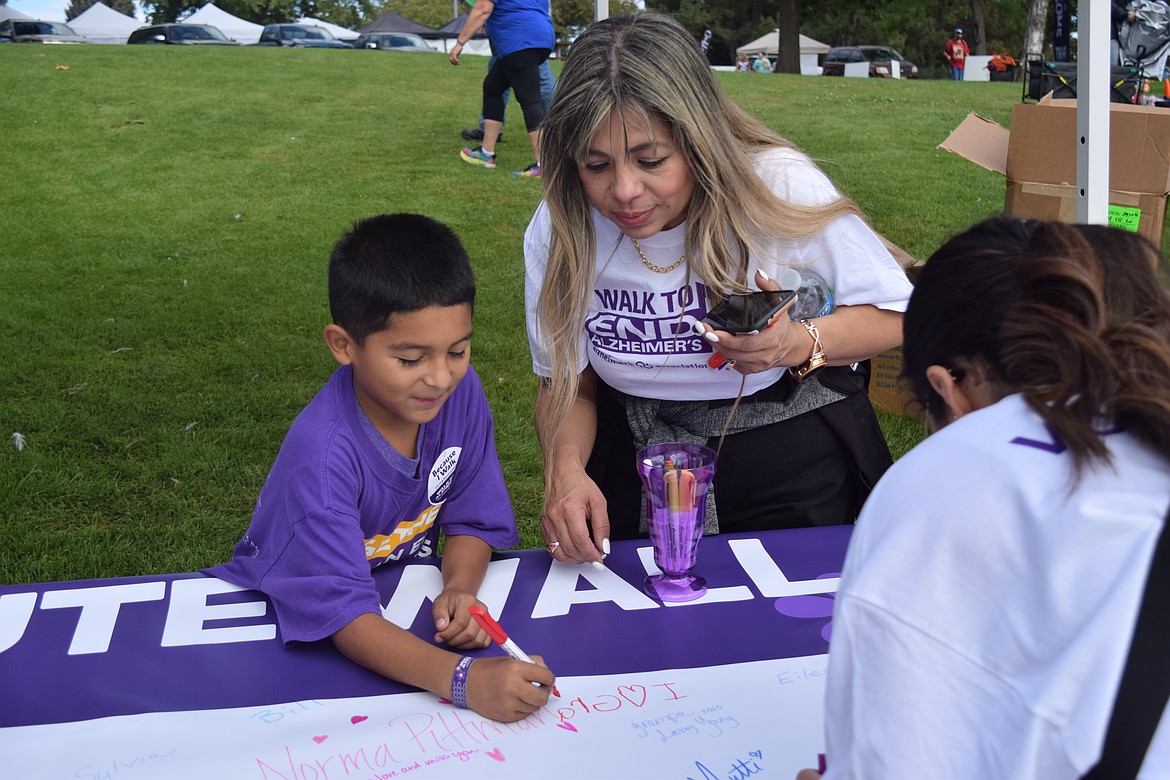 Imelda Broyles helps Santigo Melara write “I (heart) grandpa” at the walk to end Alzheimer's on Sat.