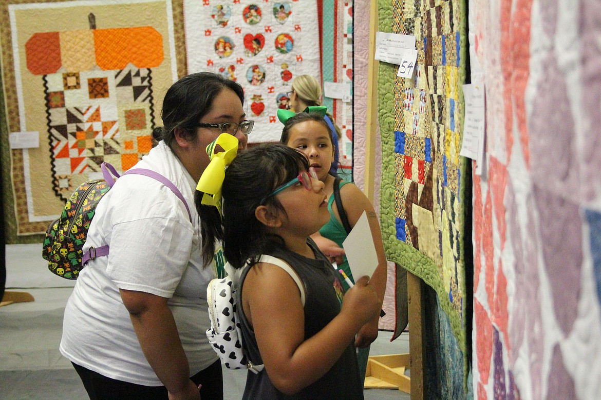 Sadie Diaz, foreground, studies a quilt while filling out her ballot at the FCAD quilt show, consulting with her mom Isabel Diaz, center and her sister Ximena Diaz, background.