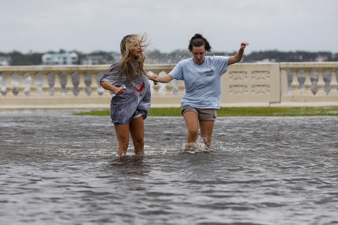 Camryn Frick, left, and Jillian Sternick, both 22, and of Tampa, hold hands as they cross a flooded street together along Bayshore Boulevard on Thursday, Sept. 26, 2024, in Tampa, Fla. (Jefferee Woo/Tampa Bay Times via AP)