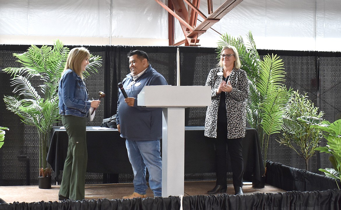 Outgoing Moses Lake Chamber of Commerce Board Chair Jason Avila passes the gavel and microphone to incoming Chair Kim Pope, left, as Chamber Director and President Debbie Doran-Martinez, right, looks on.