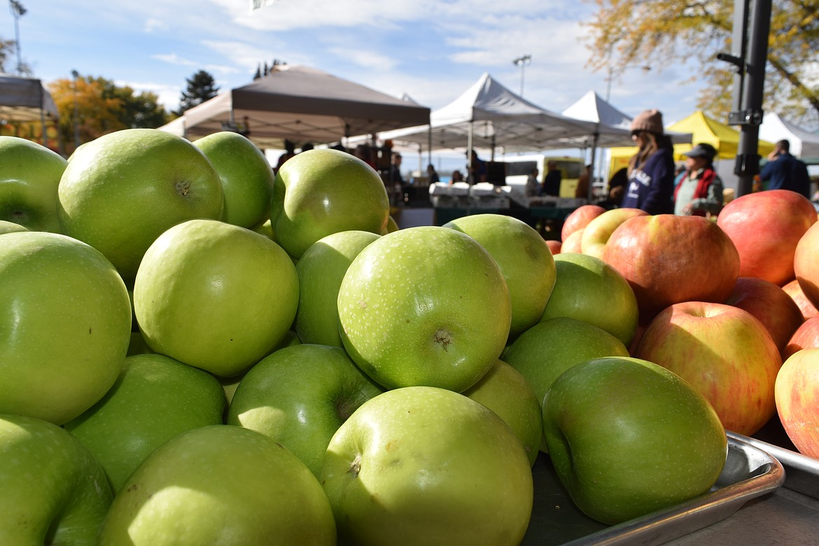 Dozens of apples are stacked for customers at the Moses Lake Farmers Market, as customers wander by.