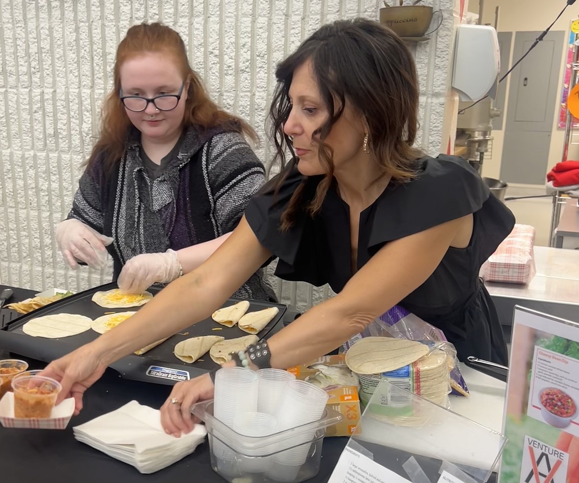 University of Idaho Professor Shelly Johnson assists Venture Academy High School student Shelby Dailey as she showcases her cooking skills at Exhibit Night after spending three weeks in Johnson’s nutrition education classes.