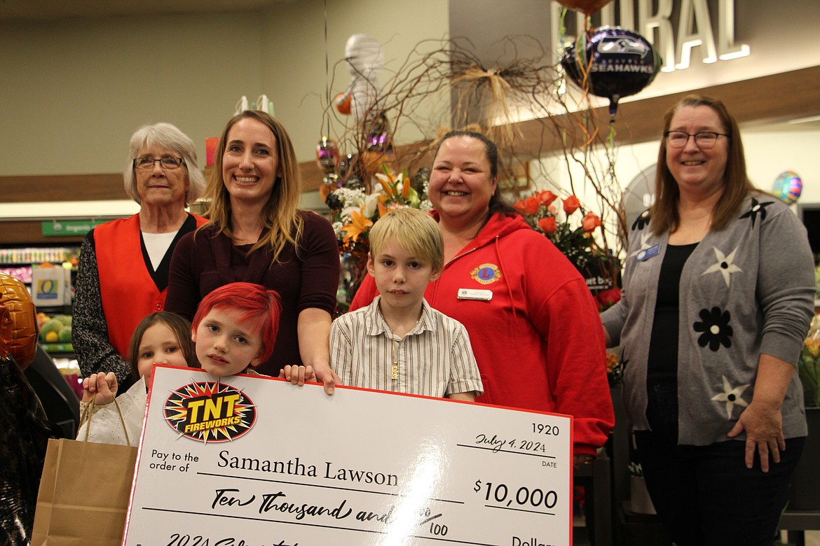 Sagle's Samantha Lawson holds a $10,000 check with her kids Ivy (6), Phoenix (7) and Loki (10) Estis inside the Safeway store she visited this summer to enter the TNT Fireworks sweepstakes. Members of the Sandpoint Lions Club, which staffed the fireworks stand this summer as a fundraiser, are pictured behind.