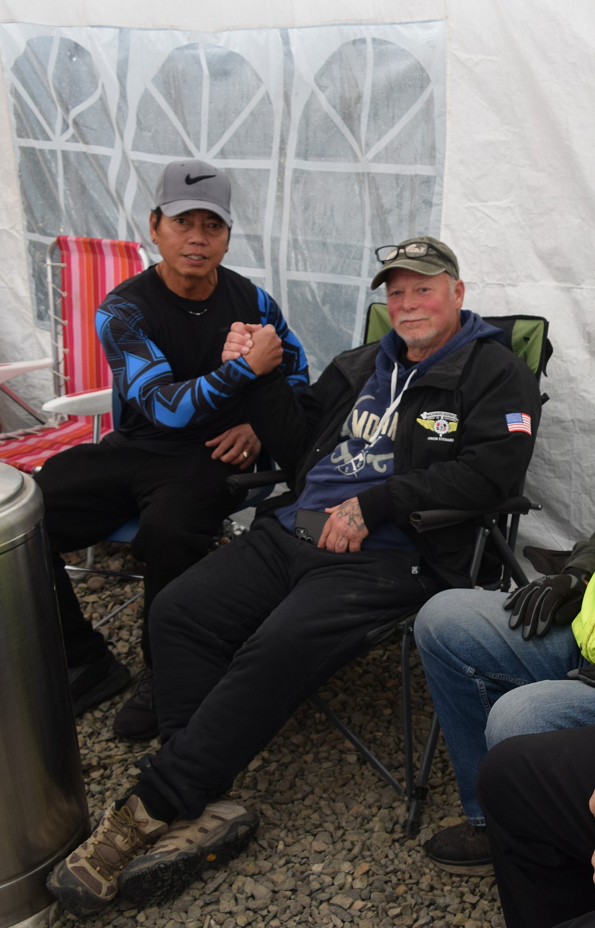 Jim Schell and Albert Llarenas shake hands while sitting at the picket line Friday. The line is still being manned 24 hours a day, seven days a week, even when the rain is pouring, and the wind is blowing.