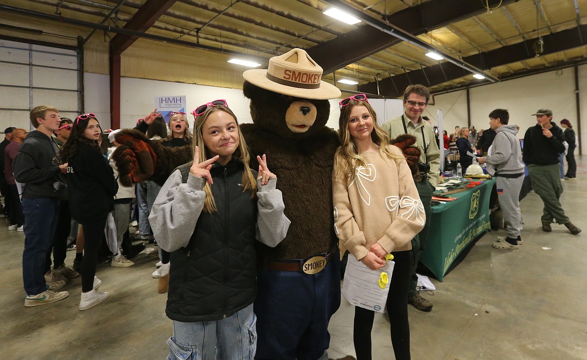 Lakeland eighth graders Clara Stoffer, left, and Lasalette Thompson stop for a photo Wednesday with Smokey Bear at the Unlock Your Future North Idaho career planning day.