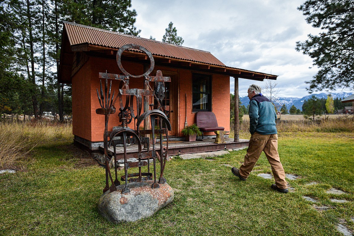 Jeffrey Funk walks to the library building on his property, part of the New Agrarian School in Bigfork on Tuesday, Nov. 12. The sculpture in the front yard was forged from wrought iron repurposed from the Old Steel Bridge by students in one of his workshops. (Casey Kreider/Daily Inter Lake)