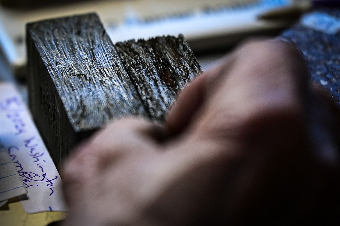 Jeffrey Funk shows two sample bars of wrought iron inside his office that have been deeply etched in acid to remove slag and reveal grain. The bar on the left is from wrought iron from the Old Steel Bridge, which used to span the Flathead River in Evergreen. The bar on the right is iron smelted from ore in his workshop. (Casey Kreider/Daily Inter Lake)