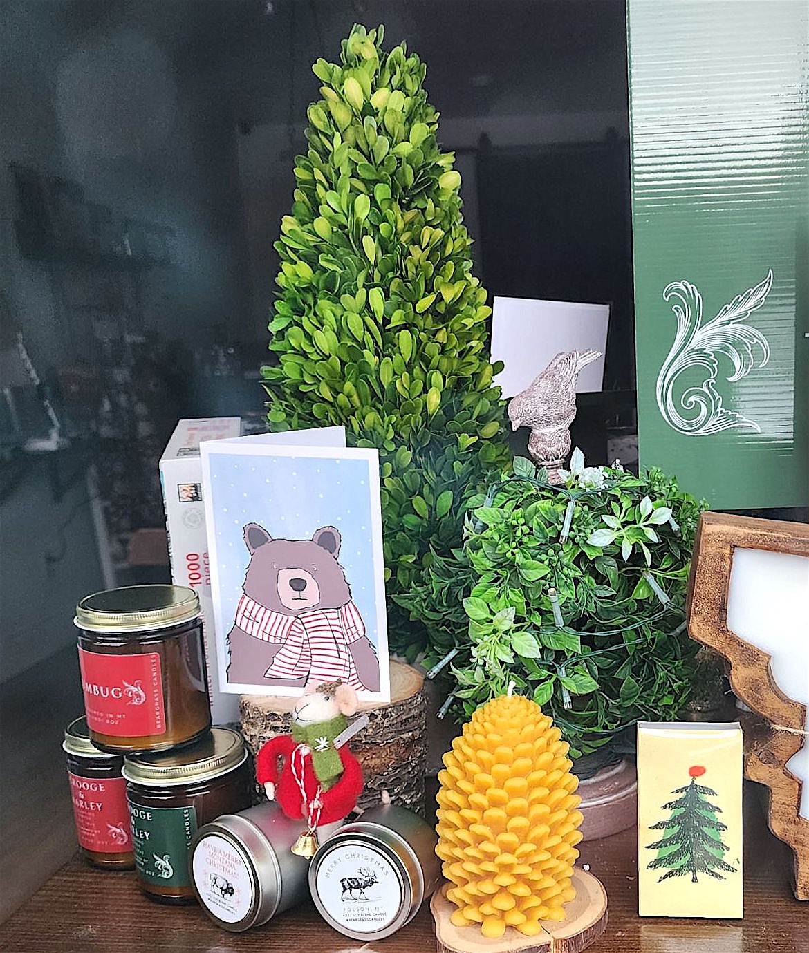 The window display at Bear Grass Candles celebrates the season with a pinecone candle, greenery, a holiday card, and jars of jam. (Berl Tiskus/Leader)