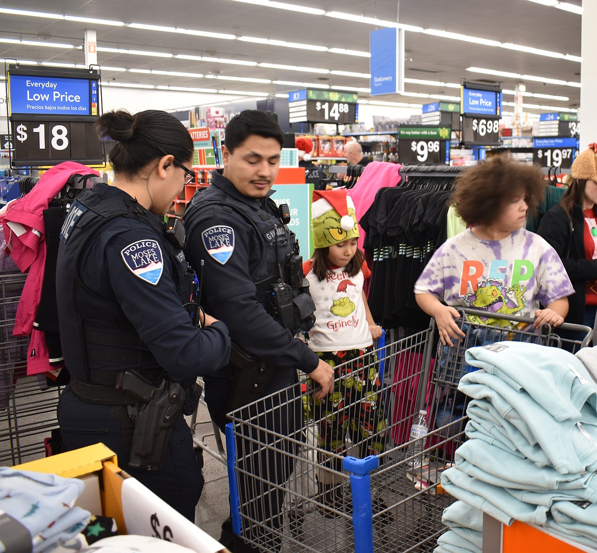 From left: Moses Lake Police Officers Yulisa Zepeda-Lopez and Greg Alvarado help Harmony Larioz, 8, and her sister Faith Larioz, 11, pick out holiday clothes at Shop with a Cop at Walmart in Moses Lake.