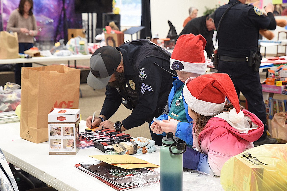 Troy Police officer Mike Roy wraps presents Dec. 12, 2024, at the Libby Assembly of God Church under the watchful eyes of Lillian Obermayer and Keagon Wesson for the Lincoln County Sheriff's Office Shop with a Cop event. (Scott Shindledecker/The Western News)