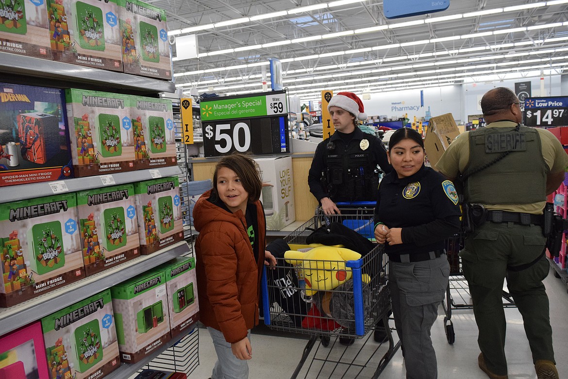 Officer Brock Denney and an Othello Police Explorer help their Shop with a Cop child pick out gifts for him and his family.