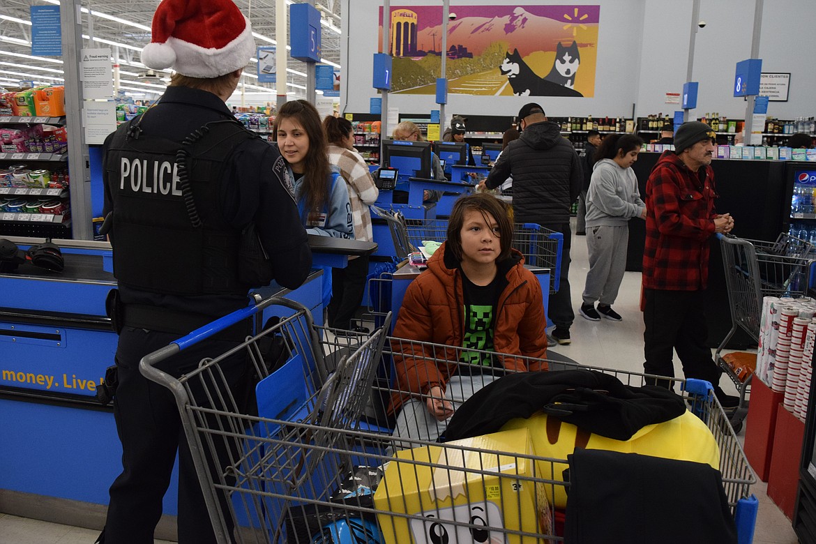 Othello Police Department officer Brock Denney checks out with a Walmart employee after the 2024 Shop with a Cop event. Denney and his shopping buddy picked out gifts for the boy and his family members Saturday.