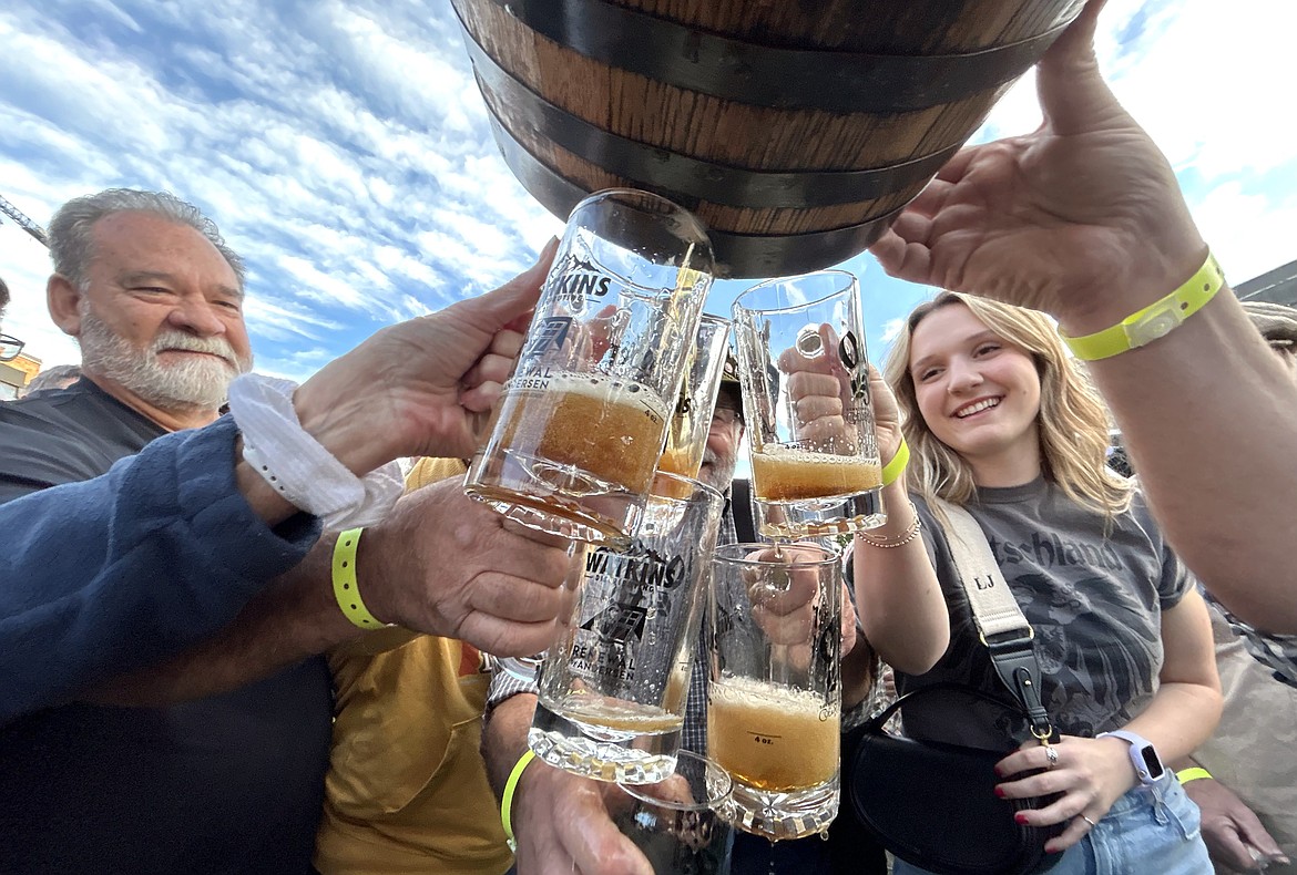 A crowd gathers around with steins to catch beer flowing from a keg on the opening day of Oktoberfest in Coeur d'Alene.