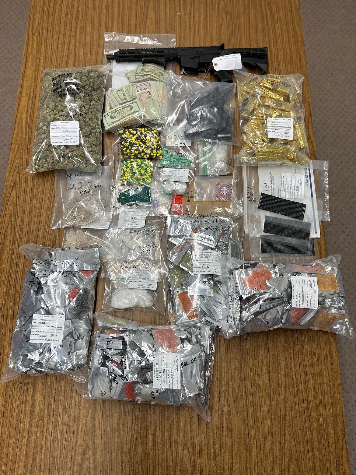 Photos of a variety of items seized during one iNET operation. In the pile of evidence are a semiautomatic rifle, thousands of dollars in cash, suspected marijuana gummies, LSD tabs, methamphetamine and other controlled substances that had not yet been identified when the photo was taken.