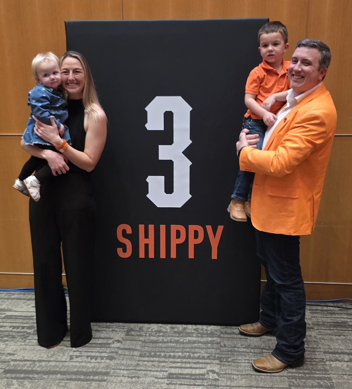 Courtesy Oklahoma State Athletics
Vanessa Shippy-Fletcher, holding daughter Hallie, and husband Matt Fletcher, holding son Luke, next to Vanessa's jersey No. 3, which will be retired by Oklahoma State softball in March.
