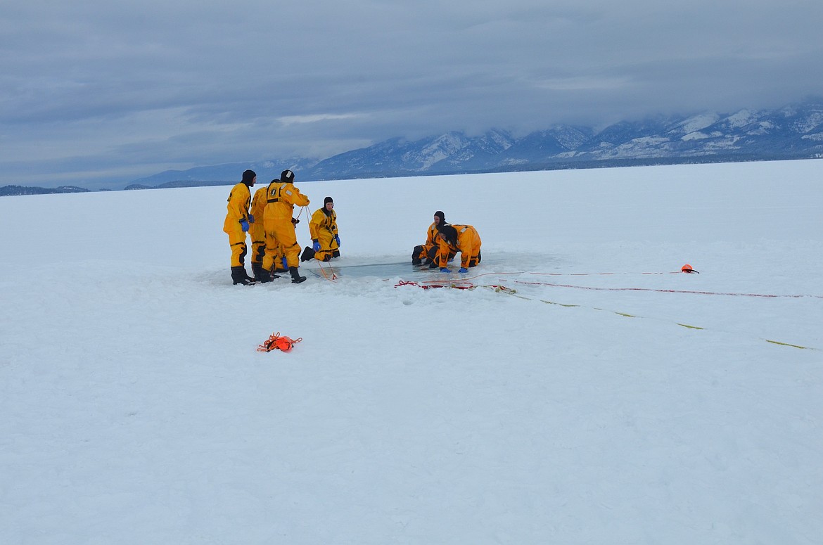 A group of volunteers huddles around a puddle of open water during an ice-rescue training Saturday on Flathead Lake.