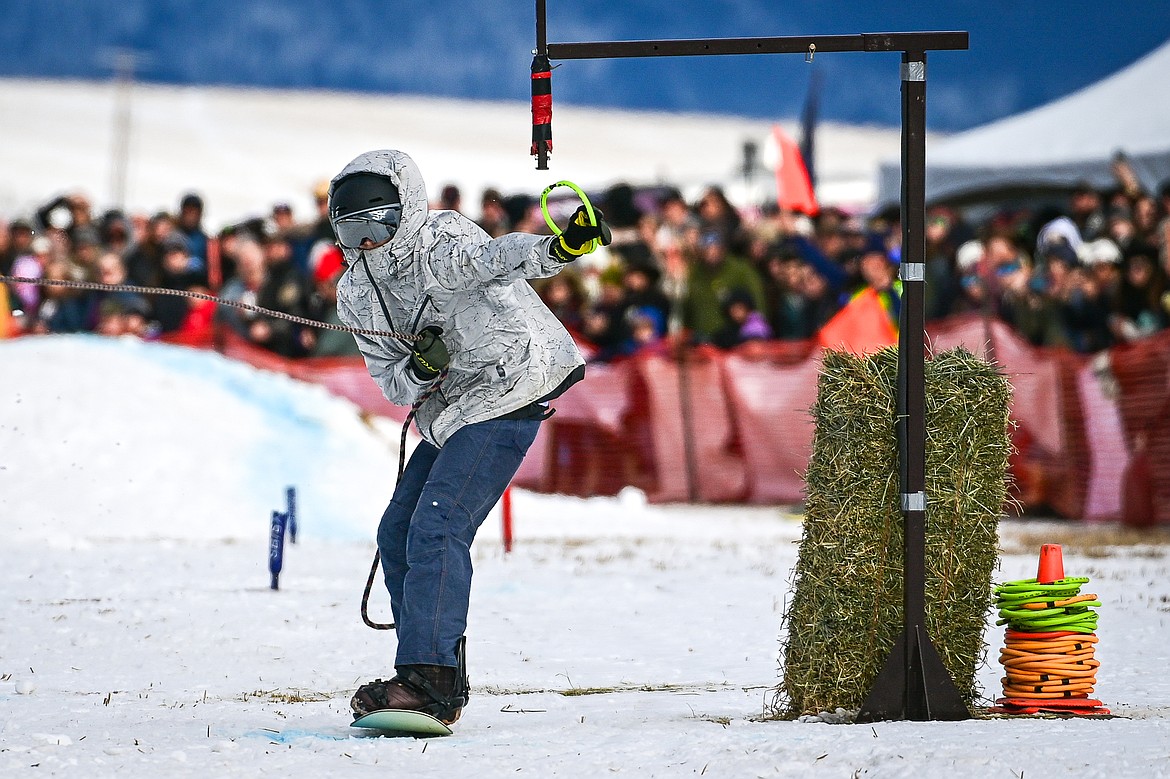 A snowboarder secures a ring as he's pulled through the course at Whitefish Skijoring on West Springcreek Road on Saturday, Feb. 22. (Casey Kreider/Daily Inter Lake)