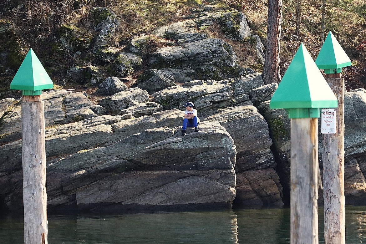 A boy sits on a rock on the shores of Lake Coeur d'Alene at Tubbs Hill.