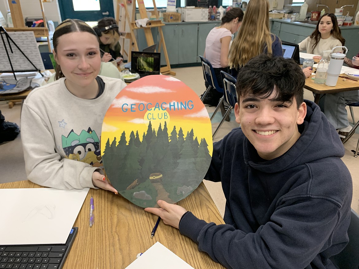 Hailie Allen and Lawyer Smith hold up the Geocaching Club sign after completing it as part of advanced painting with Cynthia Chapman at Lake City High School.