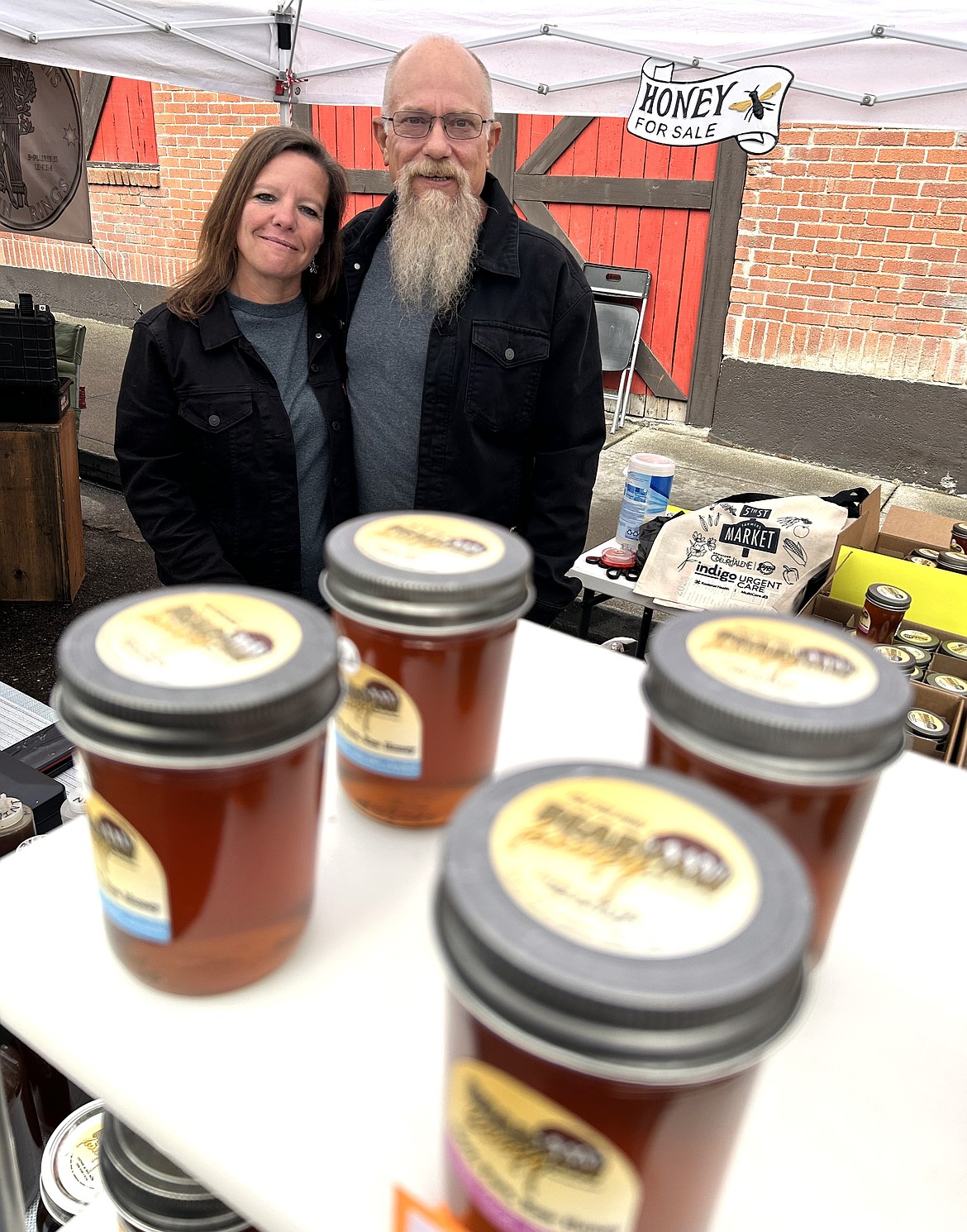 Bob and Jaymie Olmo, owners of Bear Paw Honey, pose with their products at the Fifth Street Farmers Market on Wednesday.
