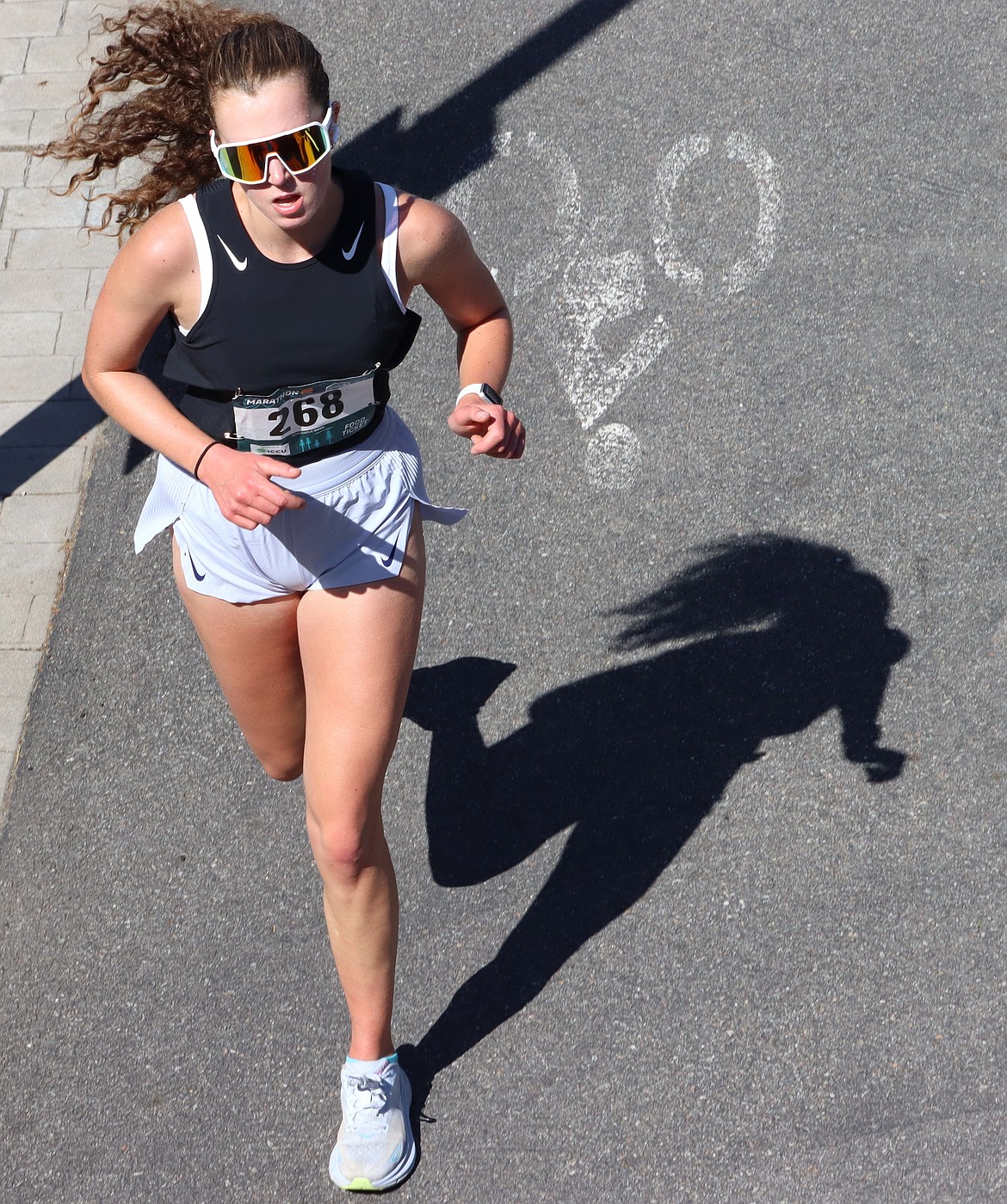 Grace Hewa of Colbert, Wash., casts a shadow as she runs in McEuen Park toward the finish of the Coeur d'Alene Marathon on Sunday. She completed the course in 3:53:07.