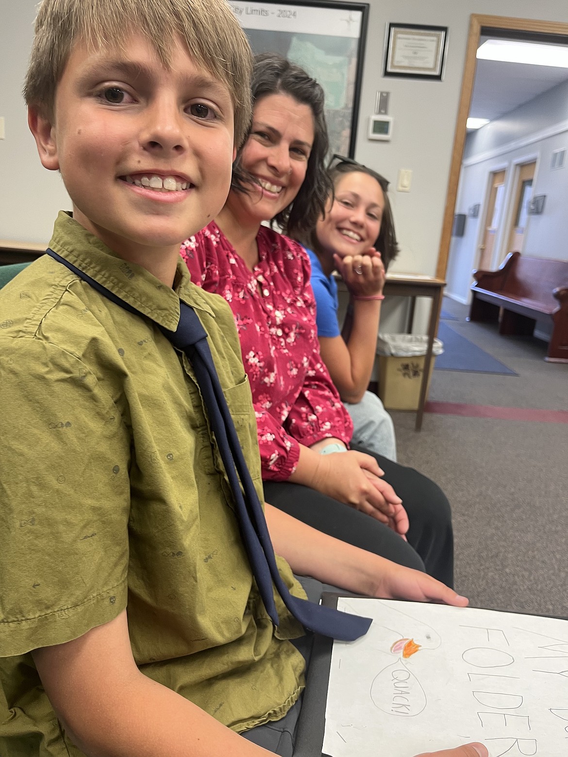 Johnny Lapotka grips his Duck Folder ("Quack" it says) after delivering his appeal to include ducks in the chicken ordinance to the Polson City Commission Monday evening. He's flanked by his support team, mom Carol Lynn and sister Cora. (Kristi Niemeyer/Leader)