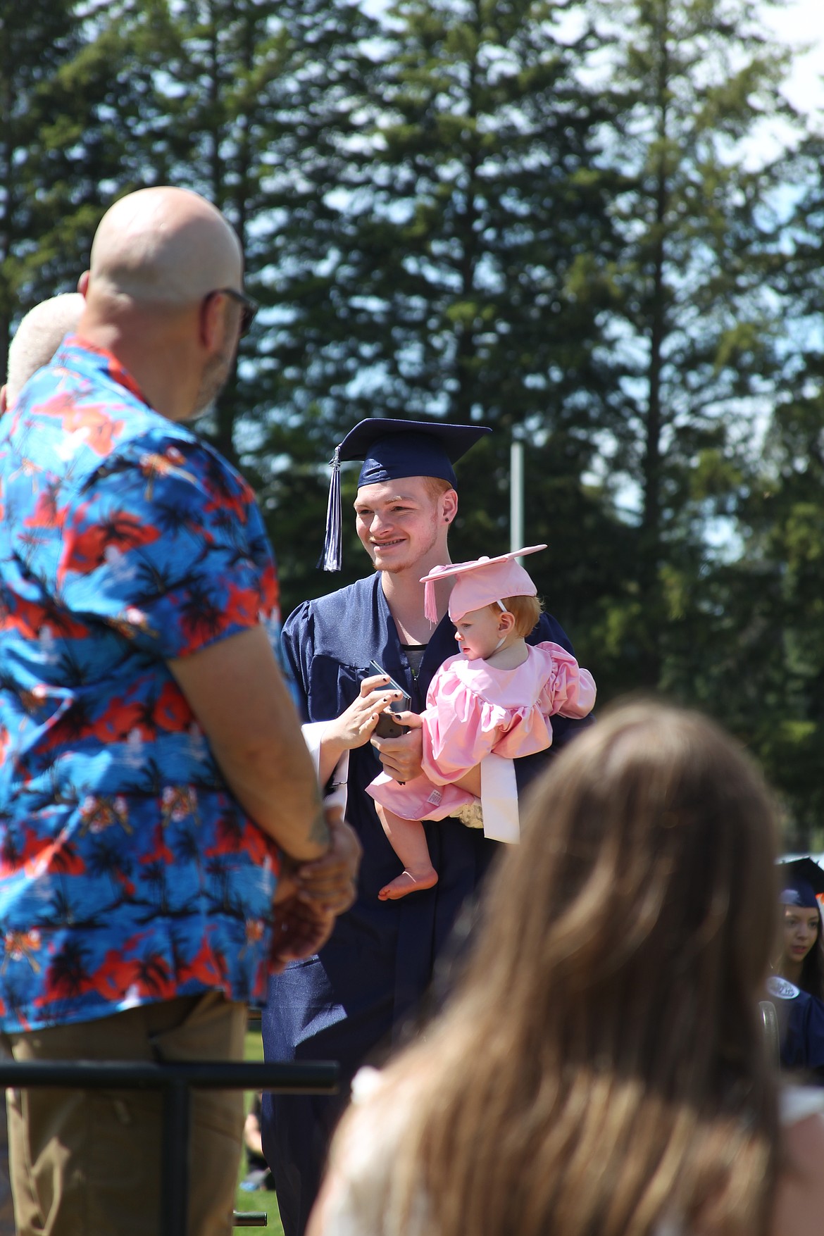 David Moore carries his daughter, Temperance, to the podium as he accepts his diploma at Saturday's Bonners Ferry High School commencement ceremony.