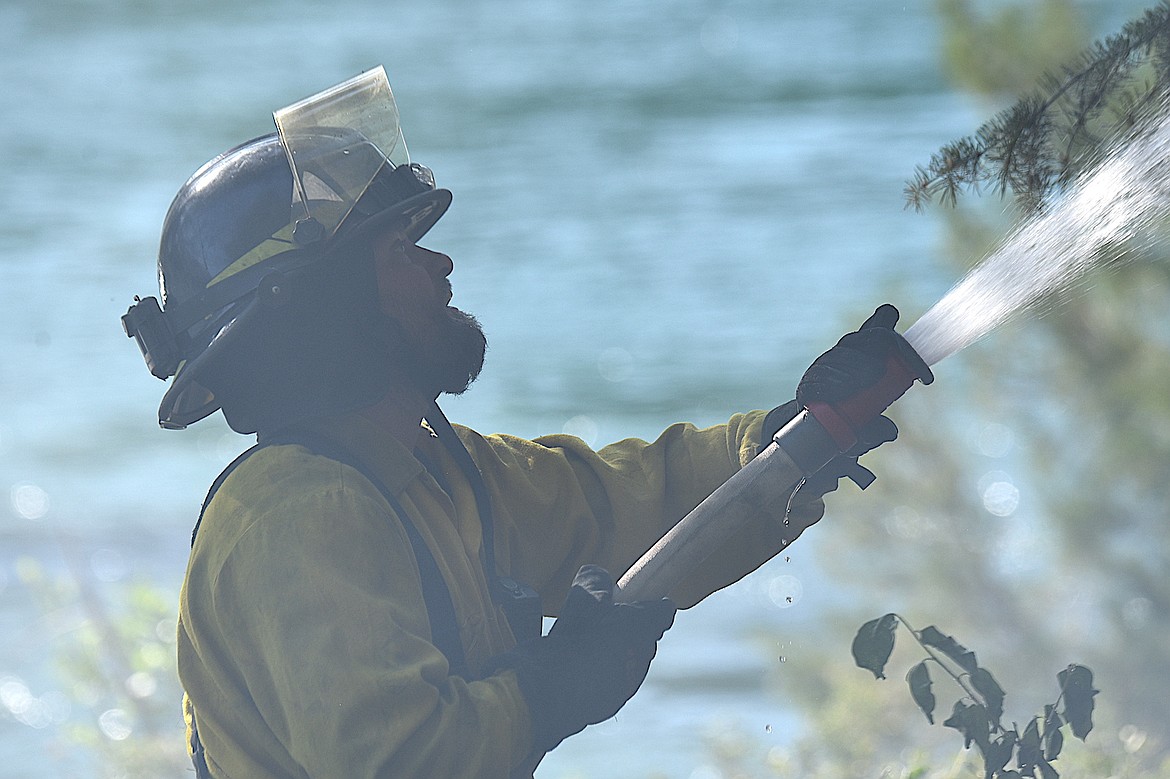 A Libby Volunteer Fire Department member Adam Orr sprays water on a wild land fire Monday, June 9, 2025, on a small strip of land between Montana 37 and the Kootenai River just below the Dunn Creek Flats Campground. (Scott Shindledecker/The Western News)