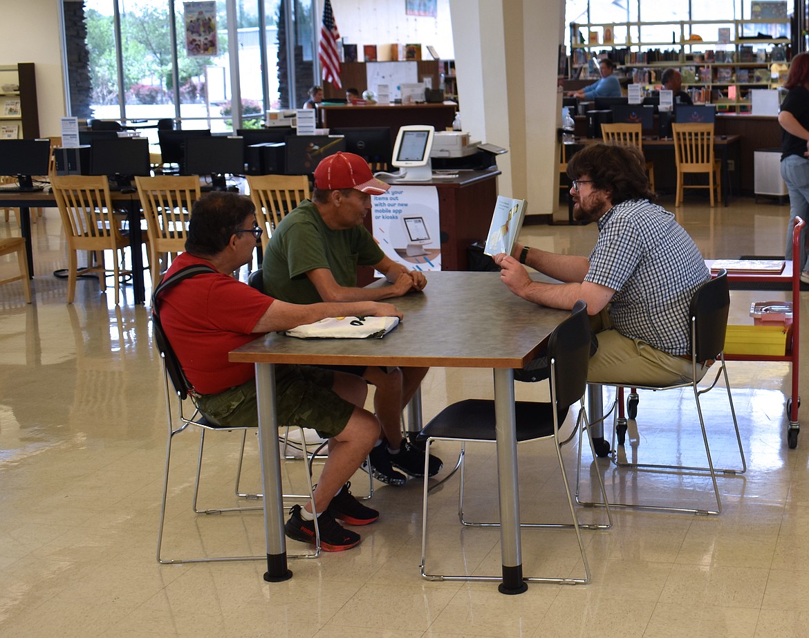 Children’s Librarian Zach Walker reads a book to David Cavazos, left, and his brother Ray Cavazos, at Adults with Special Needs Storytime at the Moses Lake Public Library.