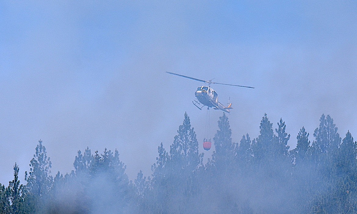 A helicopter rises above the tree line to dump water on the smoldering Wolf Syrup Fire Thursday, June 19, 2025, in Lincoln County. (Scott Shindledecker/The Western News)