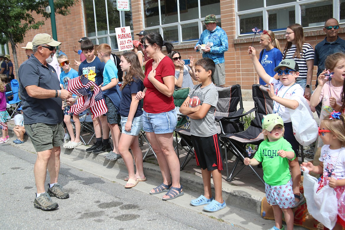 Ken Hunt, commander of VFW Post 2453, hands flags to parade-goers during the Fourth of July on Friday.