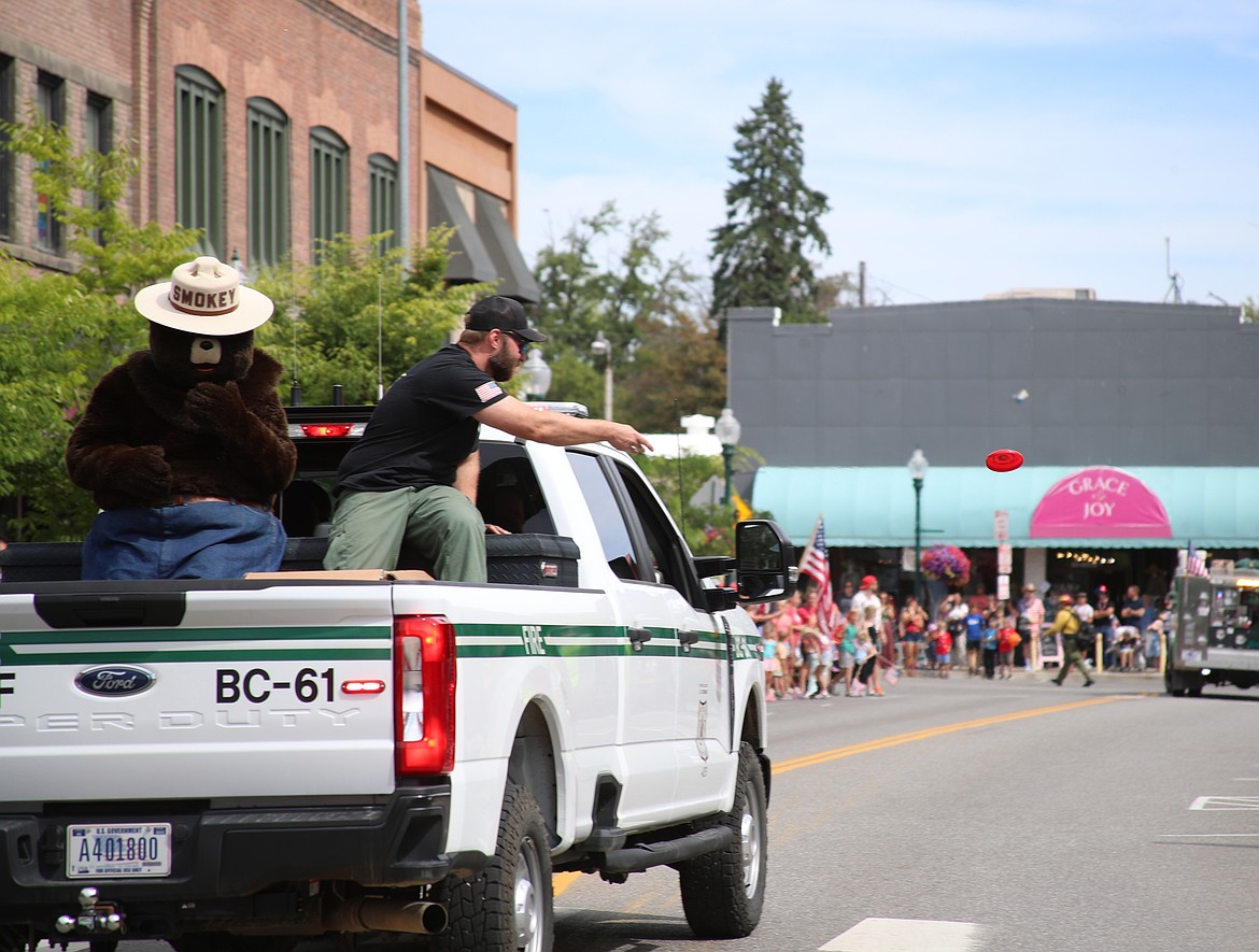 A U.S. Forest Service employee throws a small frisbee to the crowd as Smokey Bear looks on during Friday's grand parade, one of several events held by the Sandpoint Lions to celebrate the Fourth.