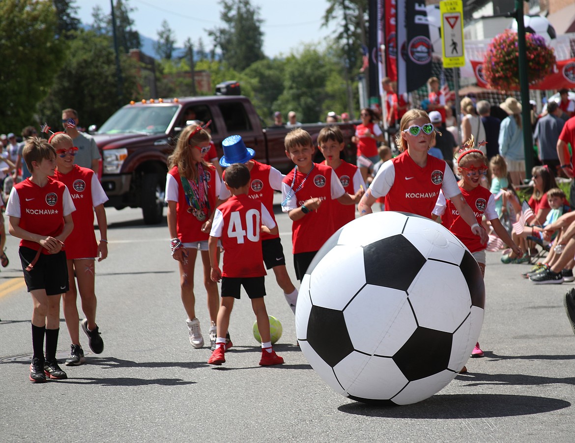 Young soccer players kick a giant inflatable soccer ball down First Avenue as they take part in the Fourth of July grand parade.