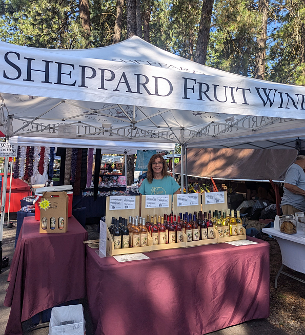 Julie Sheppard sells wines beneath Sheppard Fruit Wines' custom logoed farmers' market canopy in August 2024.