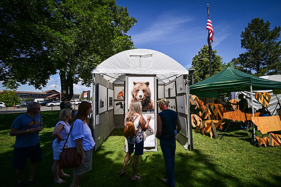 Visitors check out the work of photographer Patrick Brooks Brandenburg at the Arts in the Park festival in Depot Park in Kalispell on Friday, July 18. Kalispell's longest-running arts and music festival features a lineup of 80 juried artist booths, plein air painters, live music, food trucks and a beer and wine garden. (Casey Kreider/Daily Inter Lake)