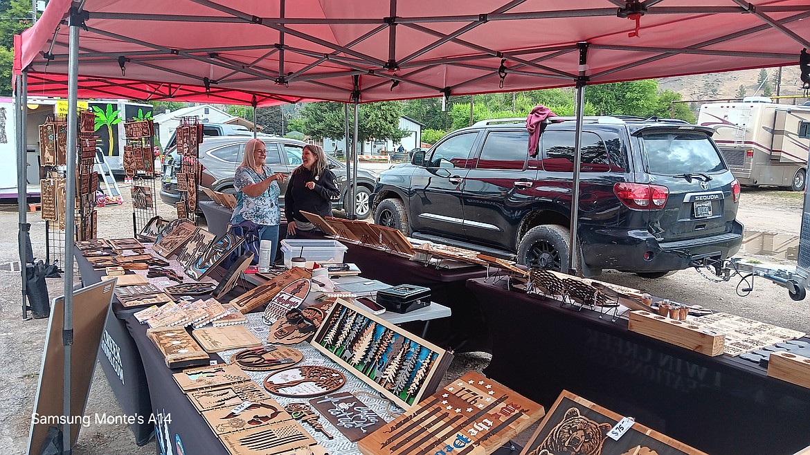 Mineral County Fair Board Chairman, Mary Jo Berry, visits with vendor Janet Hughs who owns Twin Creek Creations after the downpour Thursday to see if she had sustained any damage. Only 1 cutting board, Hughs reported. (Monte Turner/Mineral Independent)