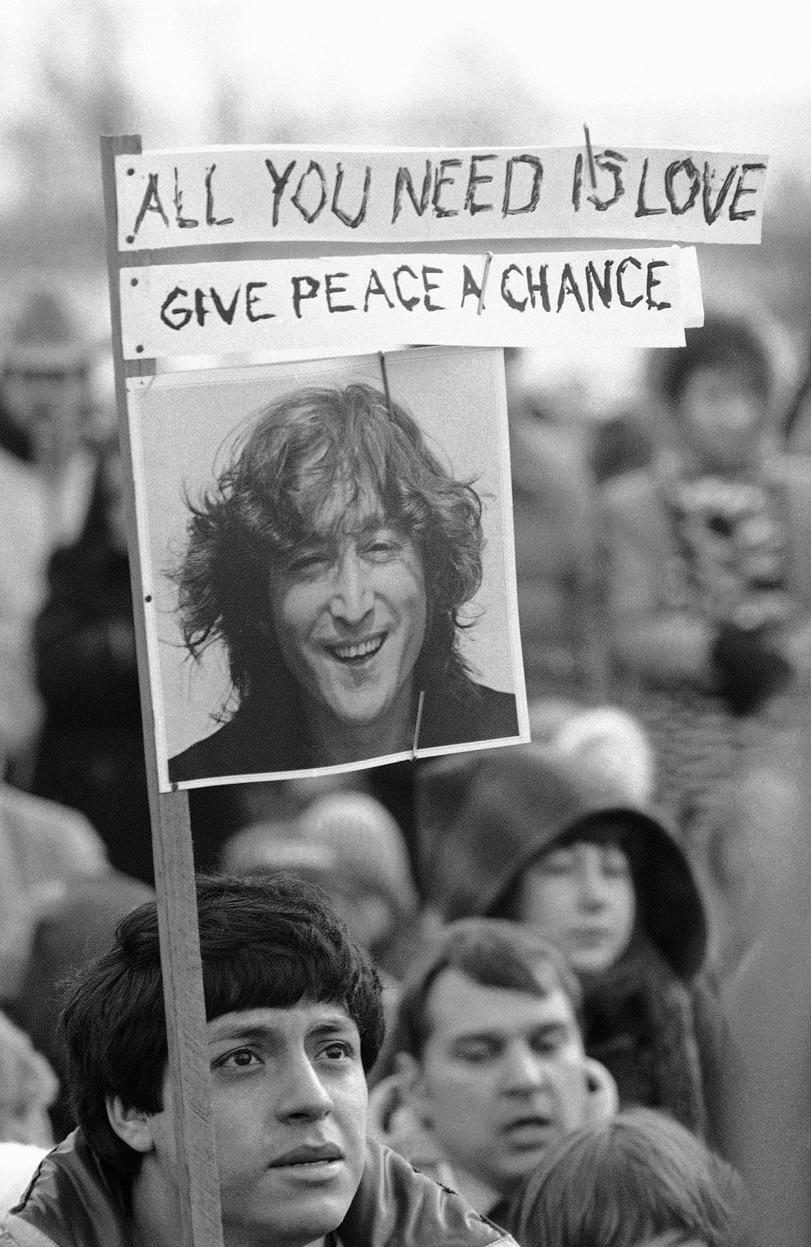 Carrying a sign emblazoned with John Lennon's picture and titles from two of his songs, a young man joins in a memorial service for the slain ex-Beatle in Chicago on Dec. 15, 1980. A crowd estimated by police to be in excess of 1,000 people listened and sang along to Lennon's songs before joining in a 10-minute period of silence asked for by his widow, Yoko Ono.